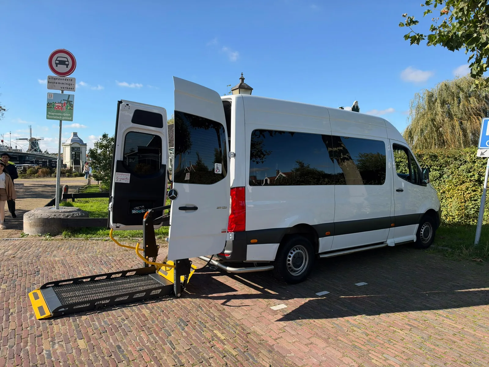 Onze witte rolstoelbus met de rolstoellift uitgeklapt naast de achterdeur